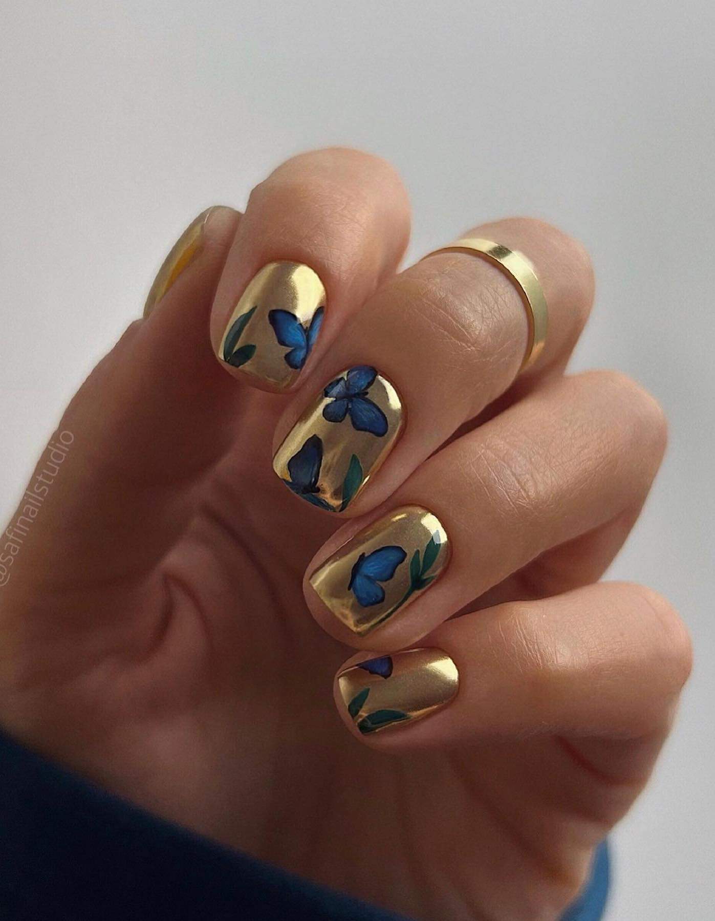 A hand with short gold nails with blue butterflies