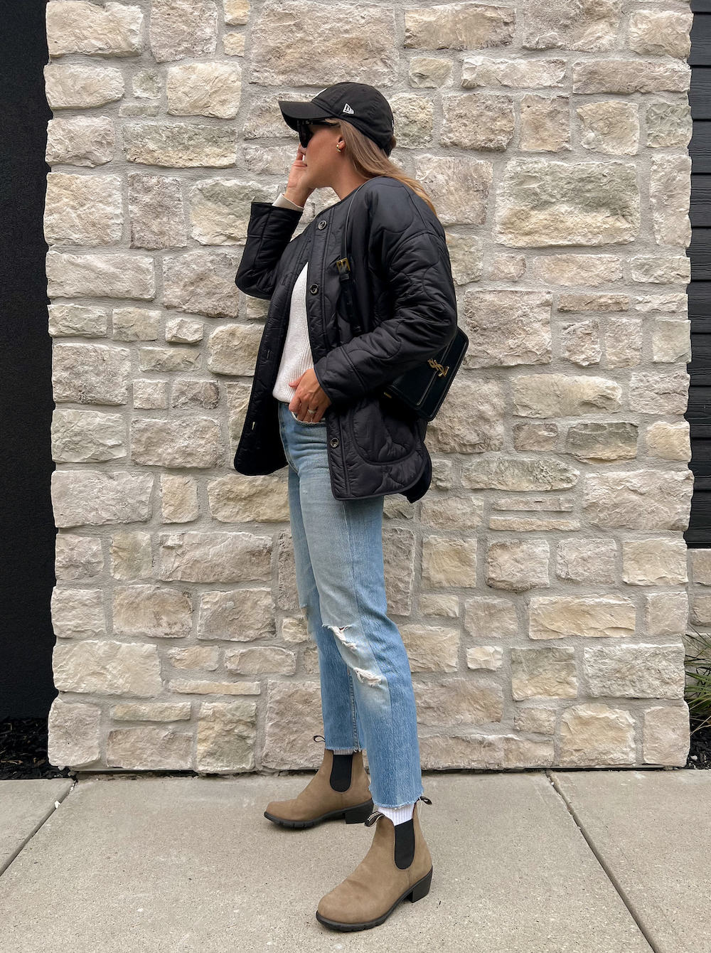 Woman wearing jeans, brown Chelsea boots, a white sweater and a black quilted jacket.
