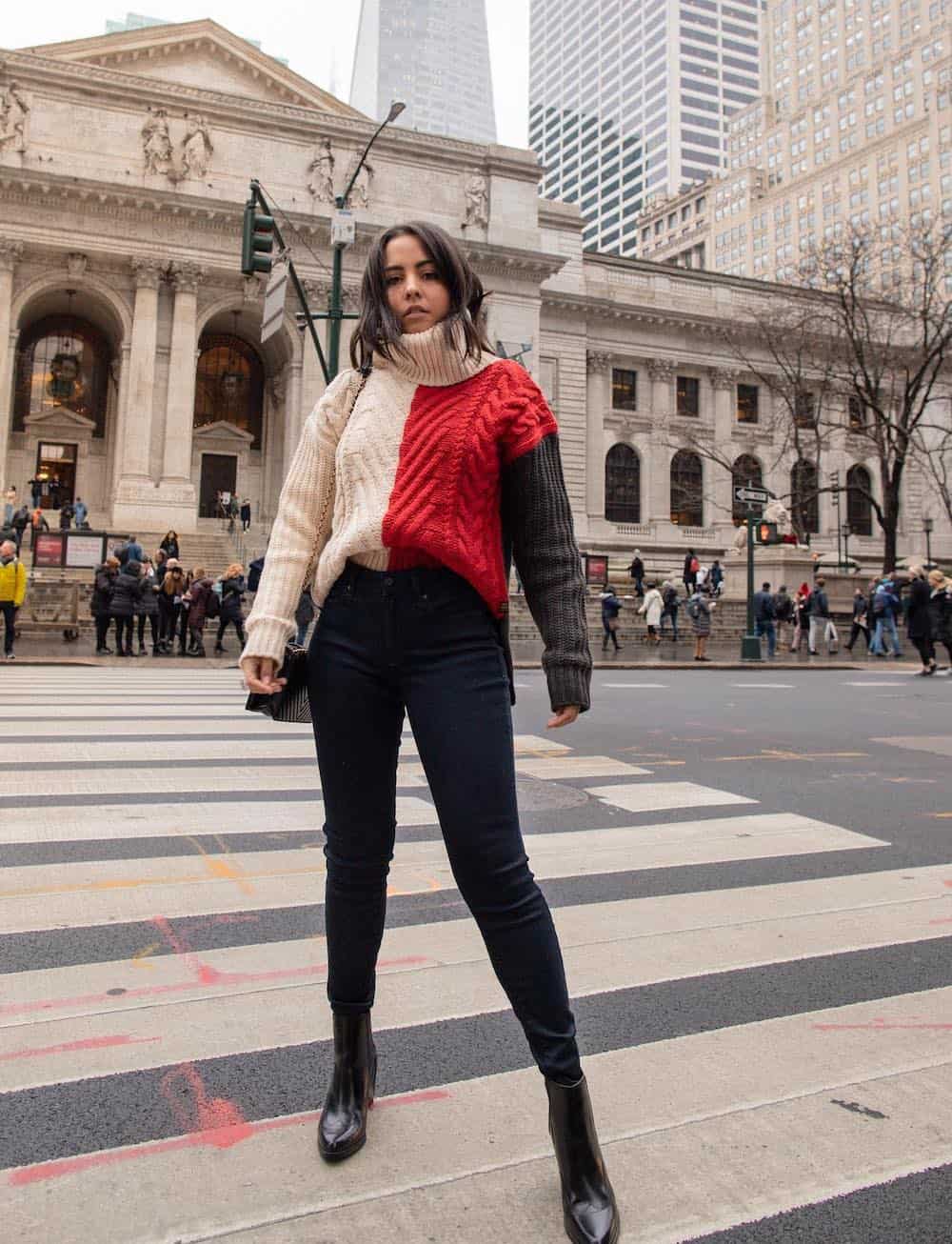 Woman wearing black skinny jeans, black boots and a color block turtleneck sweater.