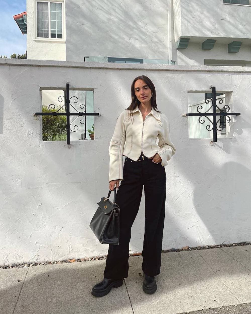 Woman wearing black pants, black chunky Chelsea boots and a cropped white leather jacket.