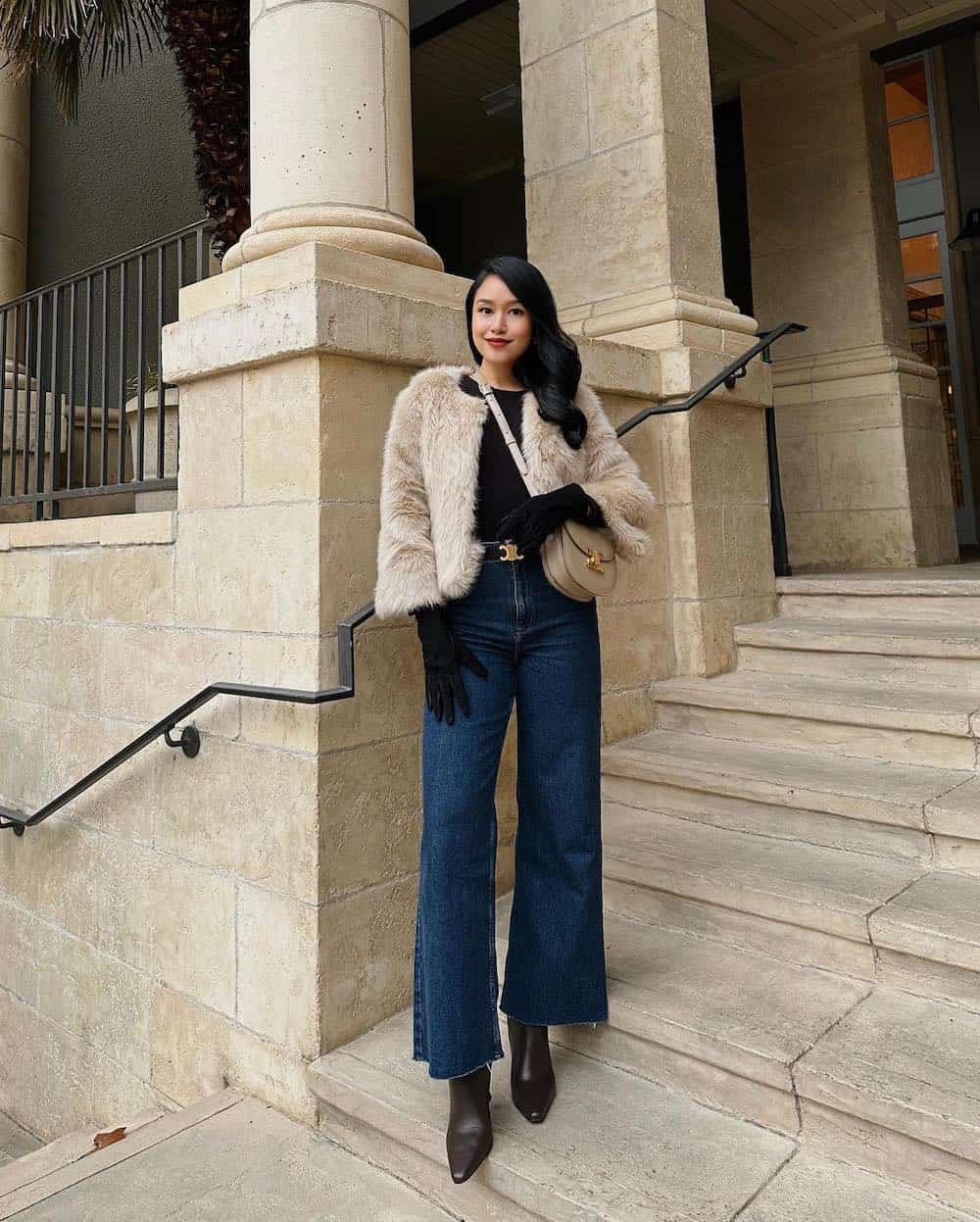 Woman wearing jeans, black boots, a black long sleeve top and a fur coat.