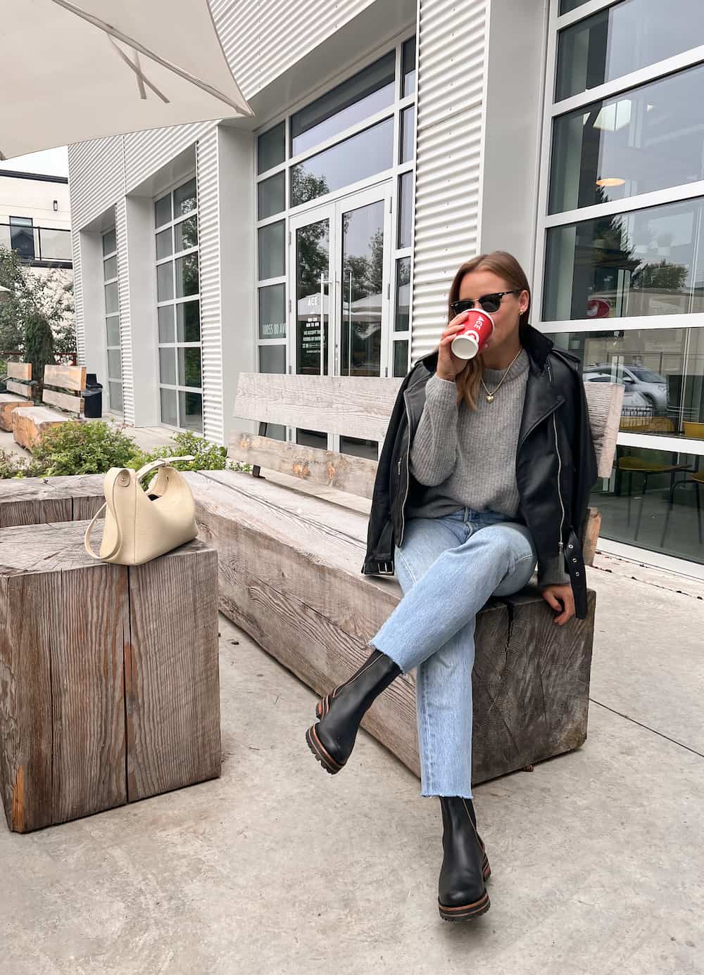 Woman wearing jeans, black chelsea boots, a grey sweater and a black leather jacket.