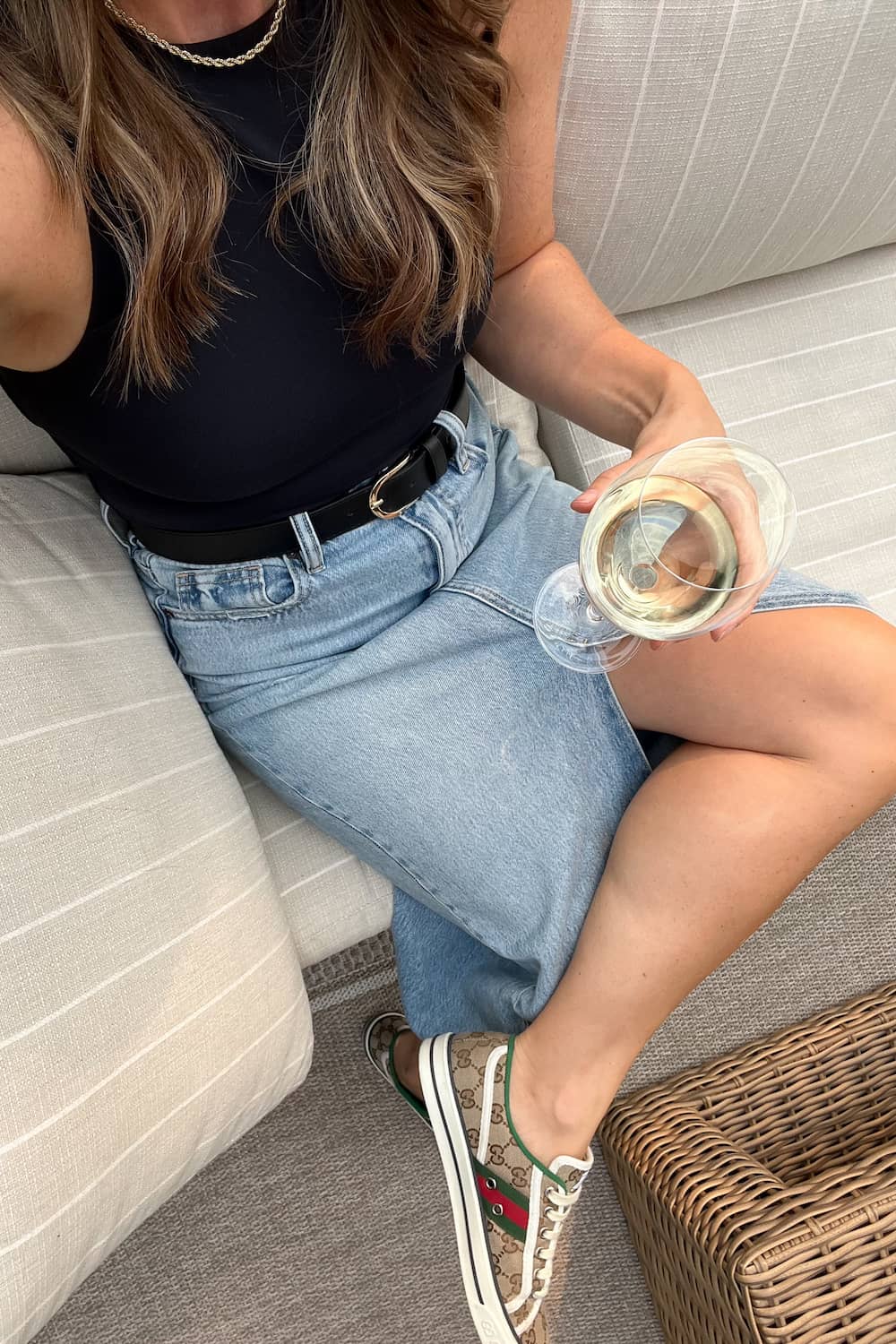 Woman wearing a long denim skirt with sneakers and a black tank top.