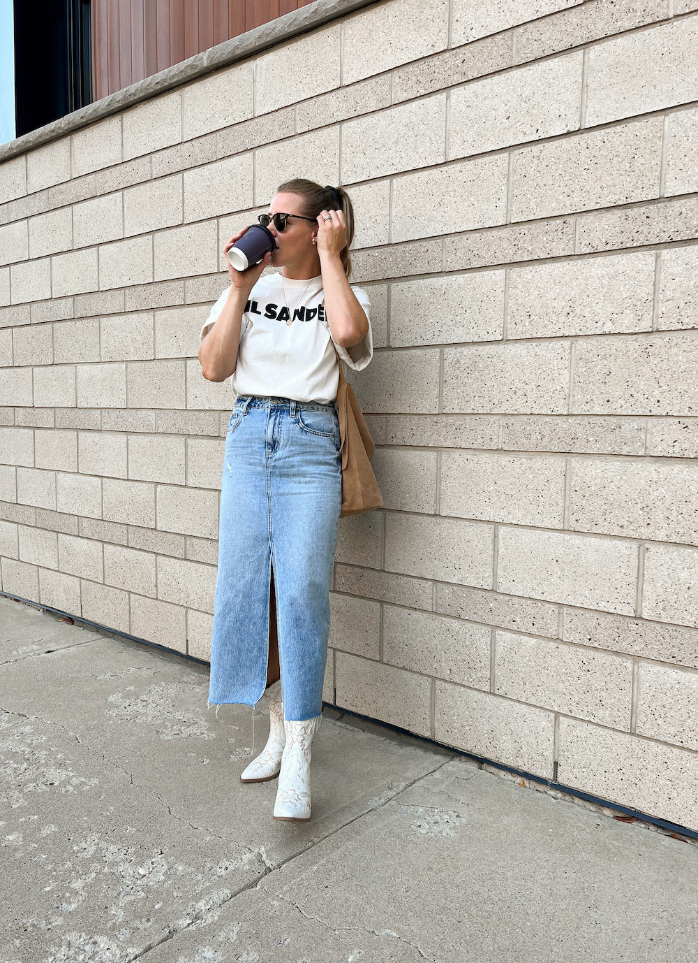 Woman wearing a long denim skirt with white cowboy boots and a graphic tee.