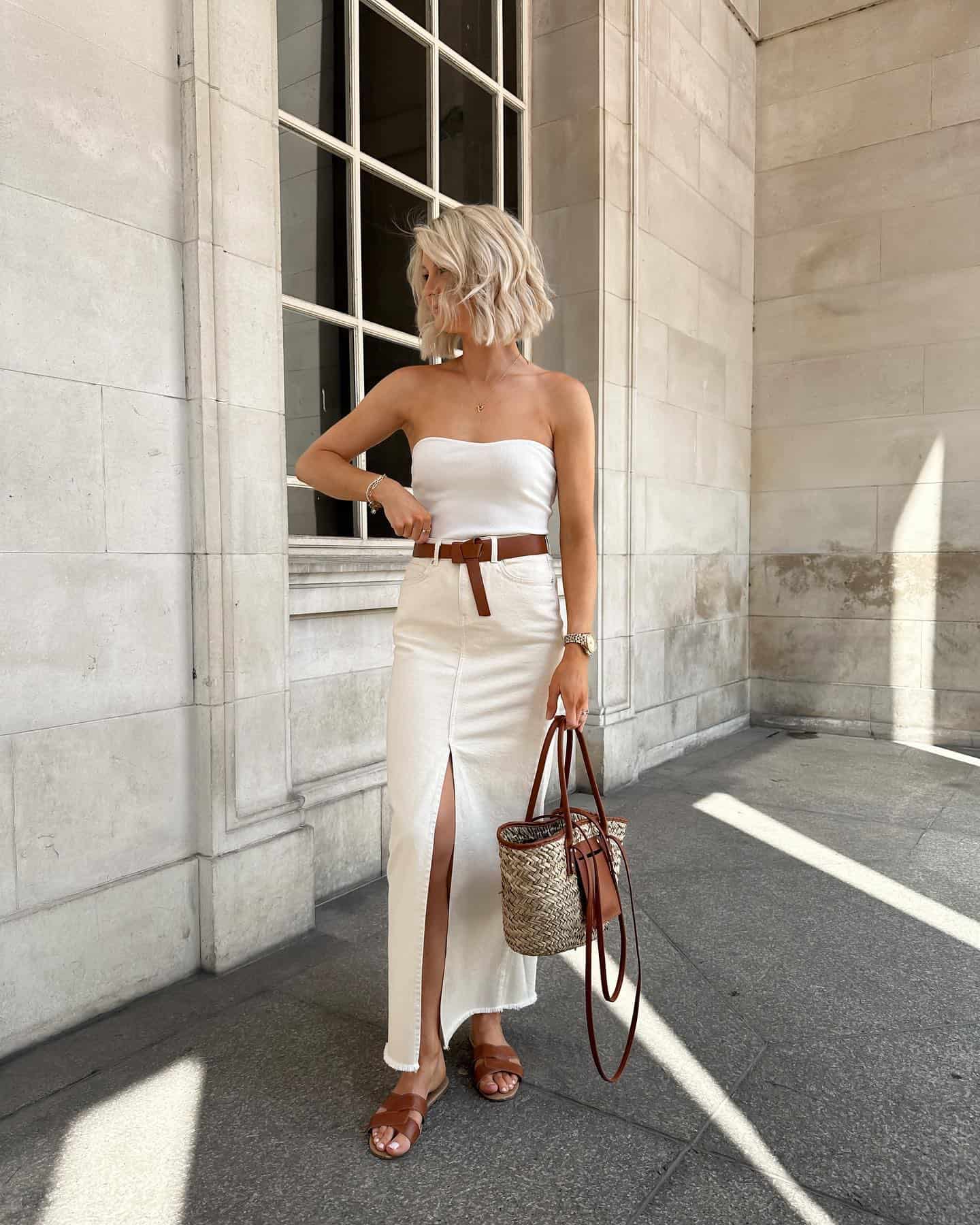 Woman wearing a white long denim skirt with a white tube top and sandals.
