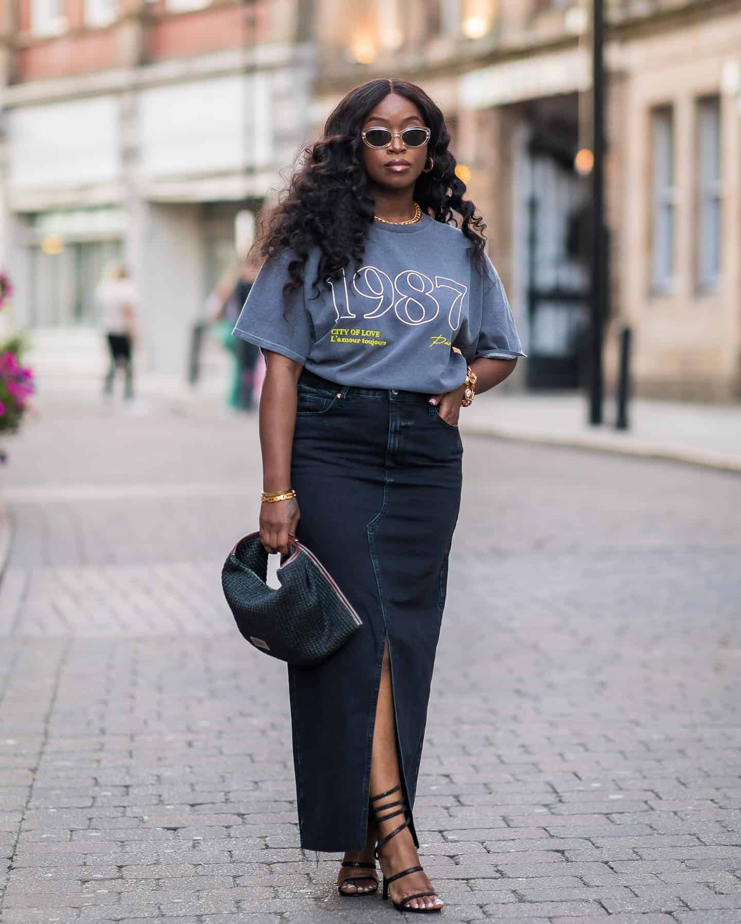 Woman wearing a long denim skirt with sandals and a graphic tee.