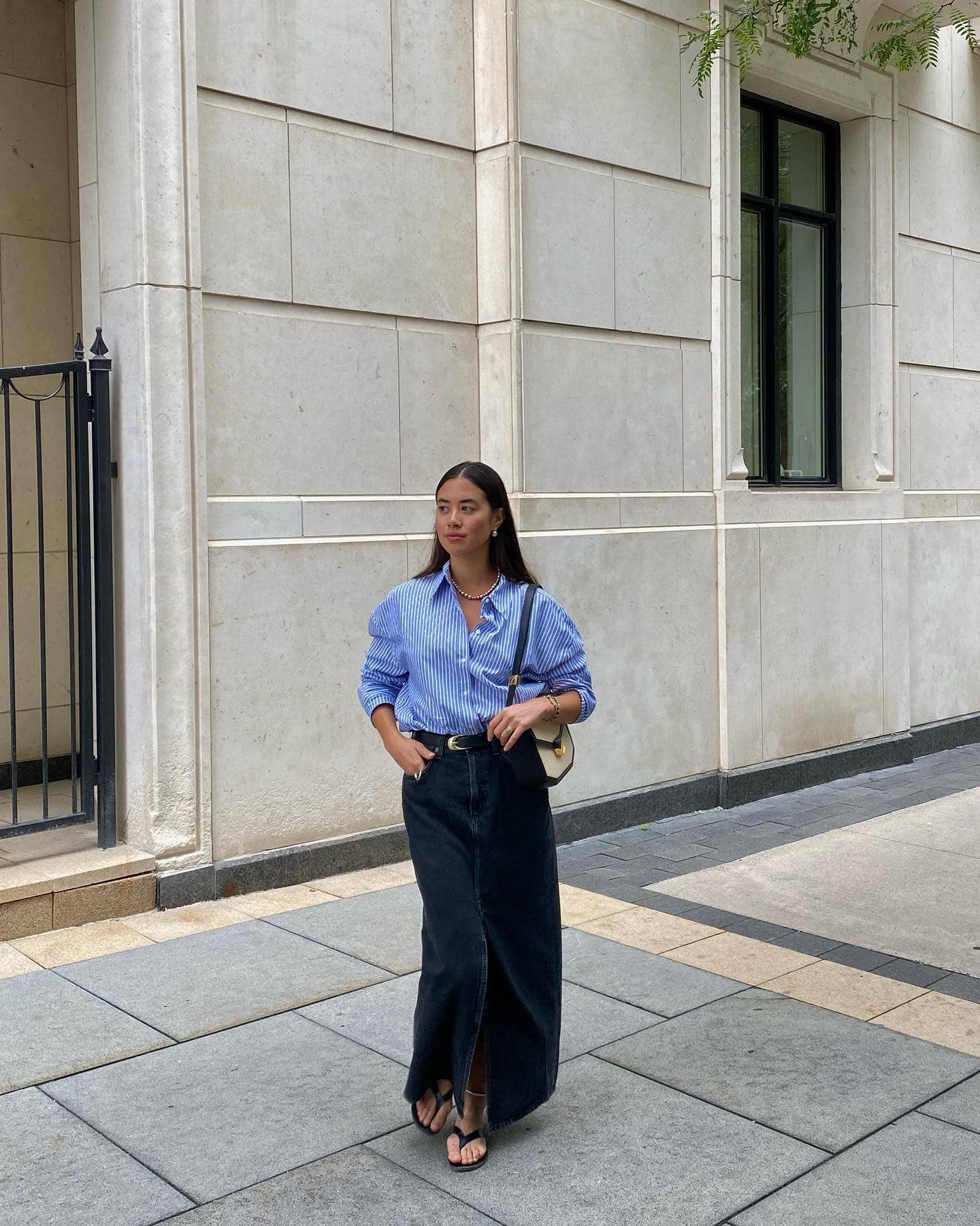 Woman wearing a long denim skirt with a button down top and sandals.