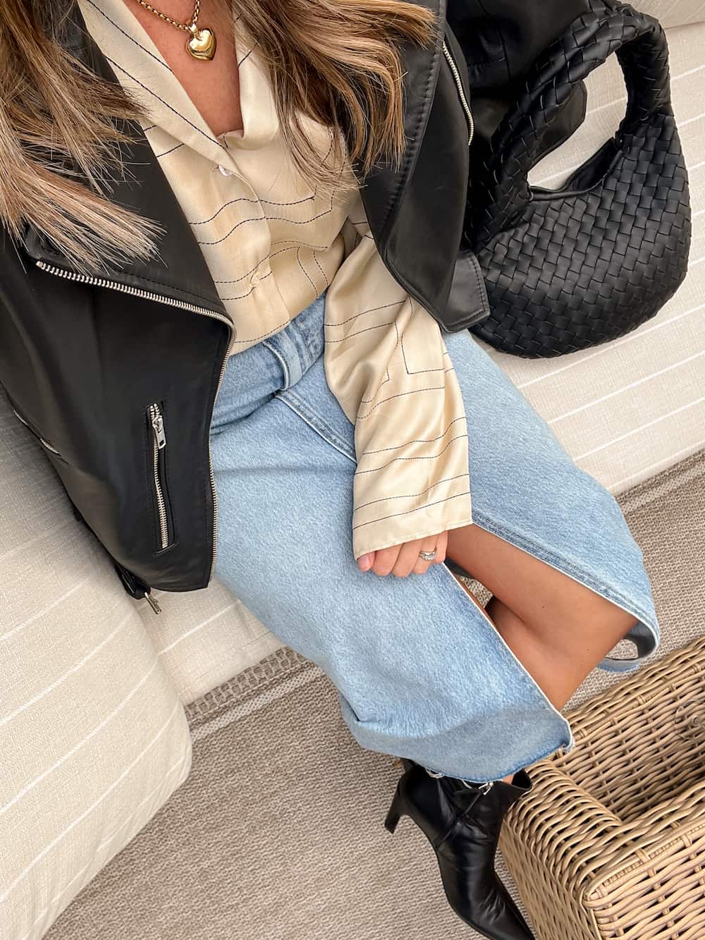 Woman wearing a long denim skirt with black boots, a silk button down top and a leather jacket.