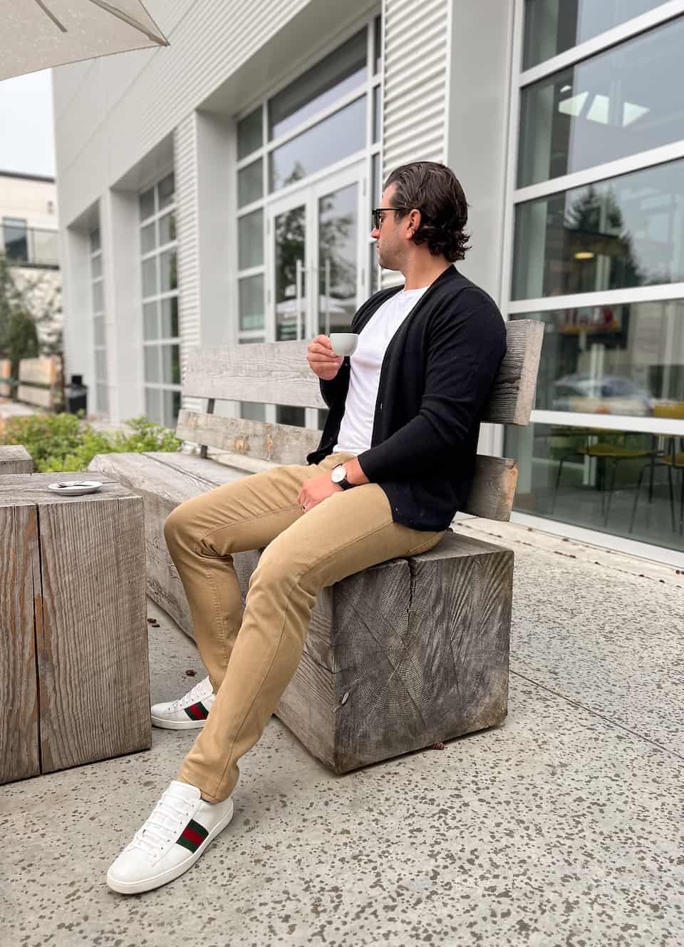 A man wearing tan chinos with a white tee, a black cardigan, and white Gucci sneakers with red and green stripes