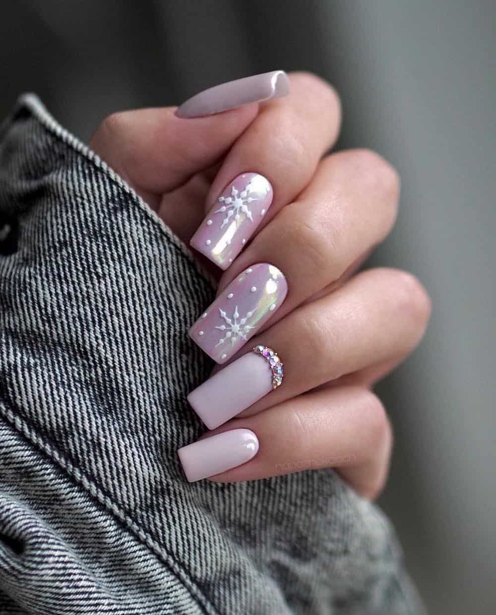 A hand with medium-long square nails with pastel pink polish, bead details, chrome accent nails, and white snowflake art