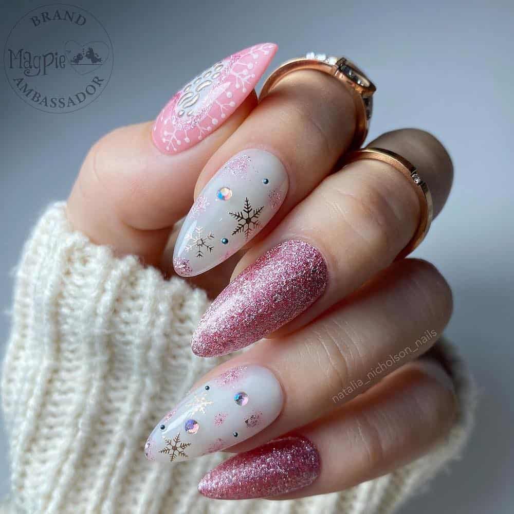 A hand with medium almond nails painted in white glossy polish and sparkly pink polish with metallic snowflakes and gems