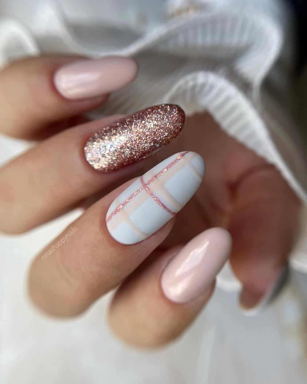 A hand with long almond nails painted with dusty pink nail polish, pink glitter, and plaid details