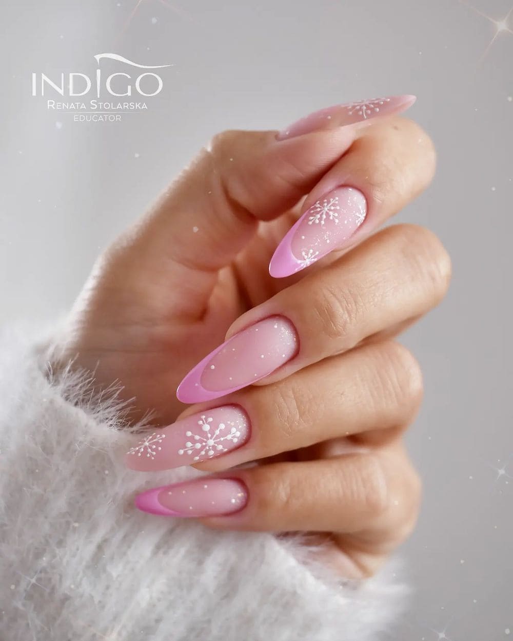 A hand with long nude almond nails with pink French tips with white dots and white snowflakes