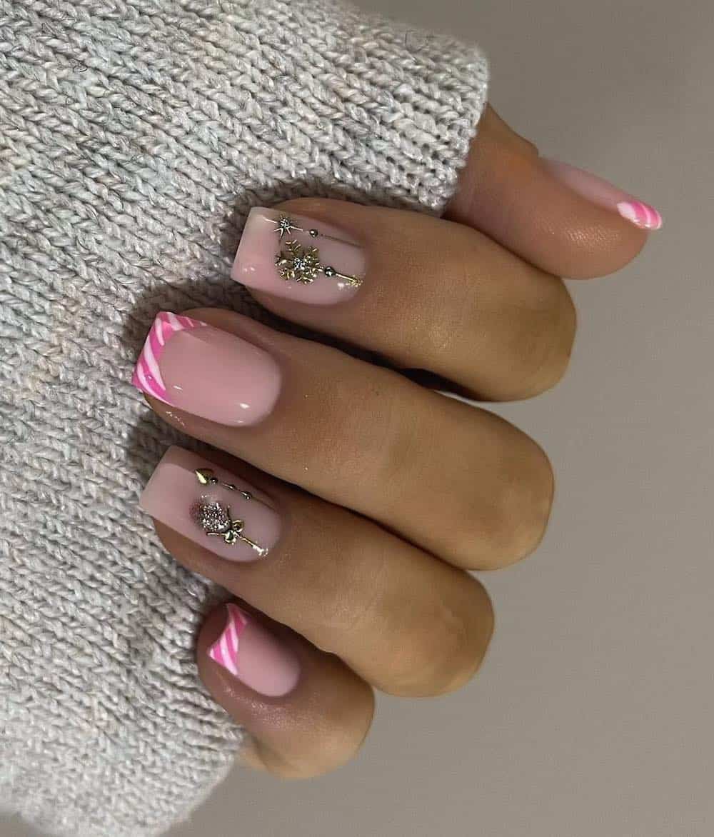 A hand with short square nails painted a glossy pink with alternating designs of pink and white striped French tips and silver gem Christmas ornaments
