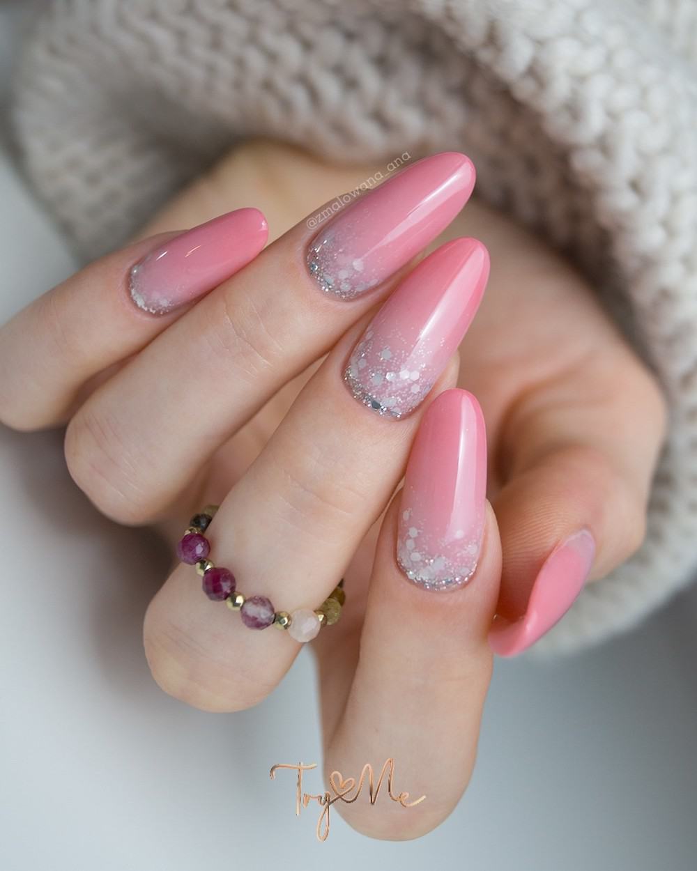 A hand with long almond nails with pink and chunky silver glitter ombre