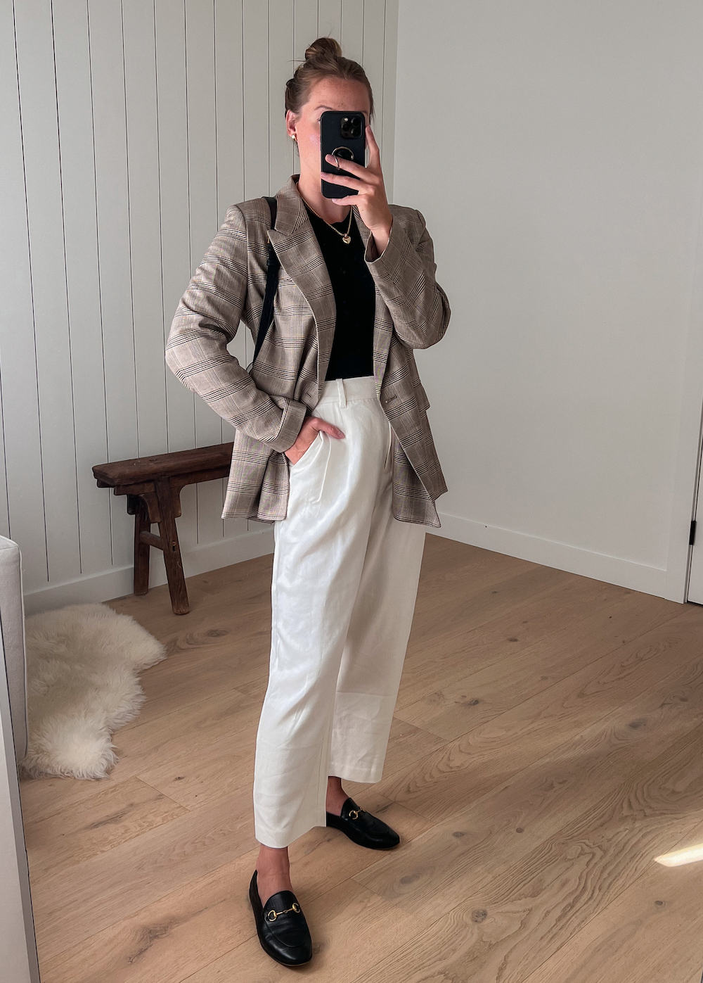 Woman wearing white trousers, a black t-shirt, black loafers and a tan plaid blazer.