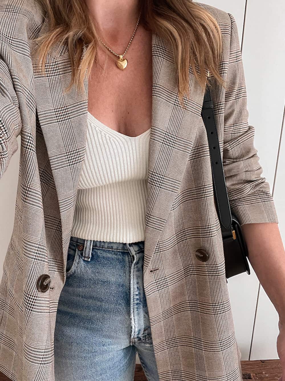 Up close photo of a woman wearing a white sweater tank top, a plaid blazer and light wash jeans.