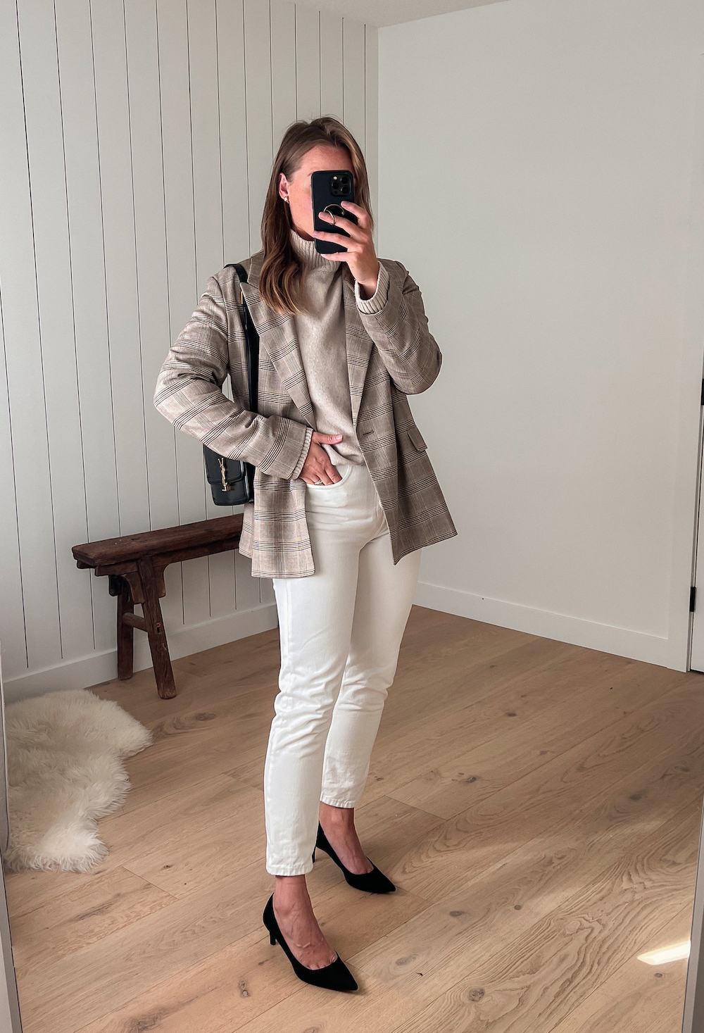 Woman wearing white jeans, a cream sweater and a tan plaid blazer with black pumps.