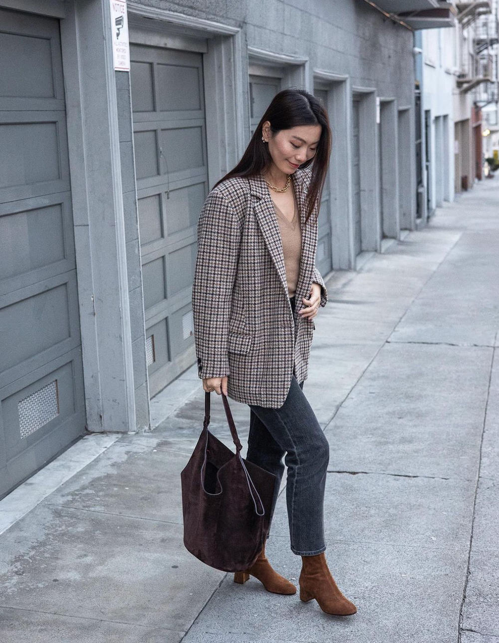 Woman wearing dark denim straight leg jeans, a brown t-shirt, a brown, grey and black plaid blazer and brown heeled booties.