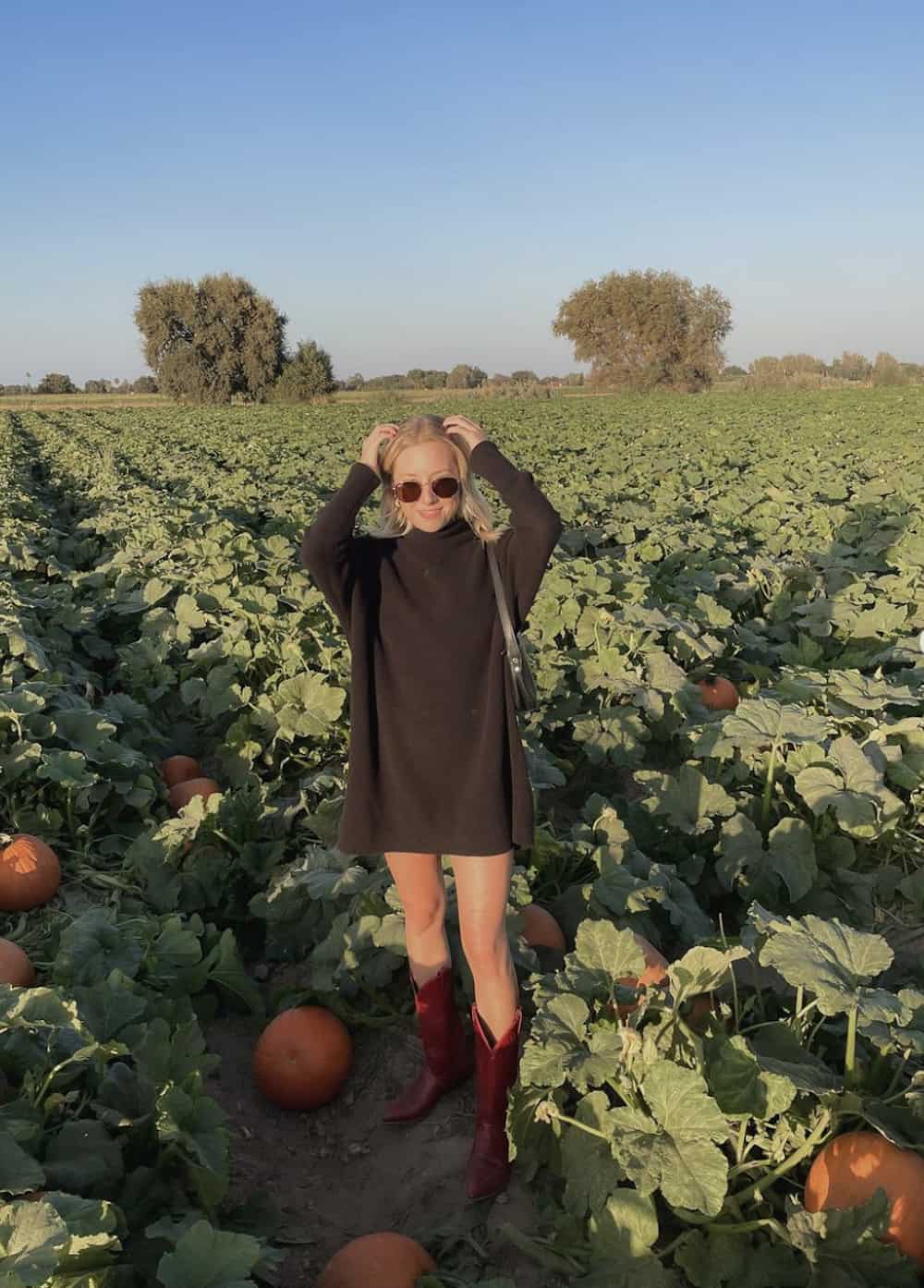 Woman wearing a black sweater dress and red cowboy boots in a pumpkin patch.