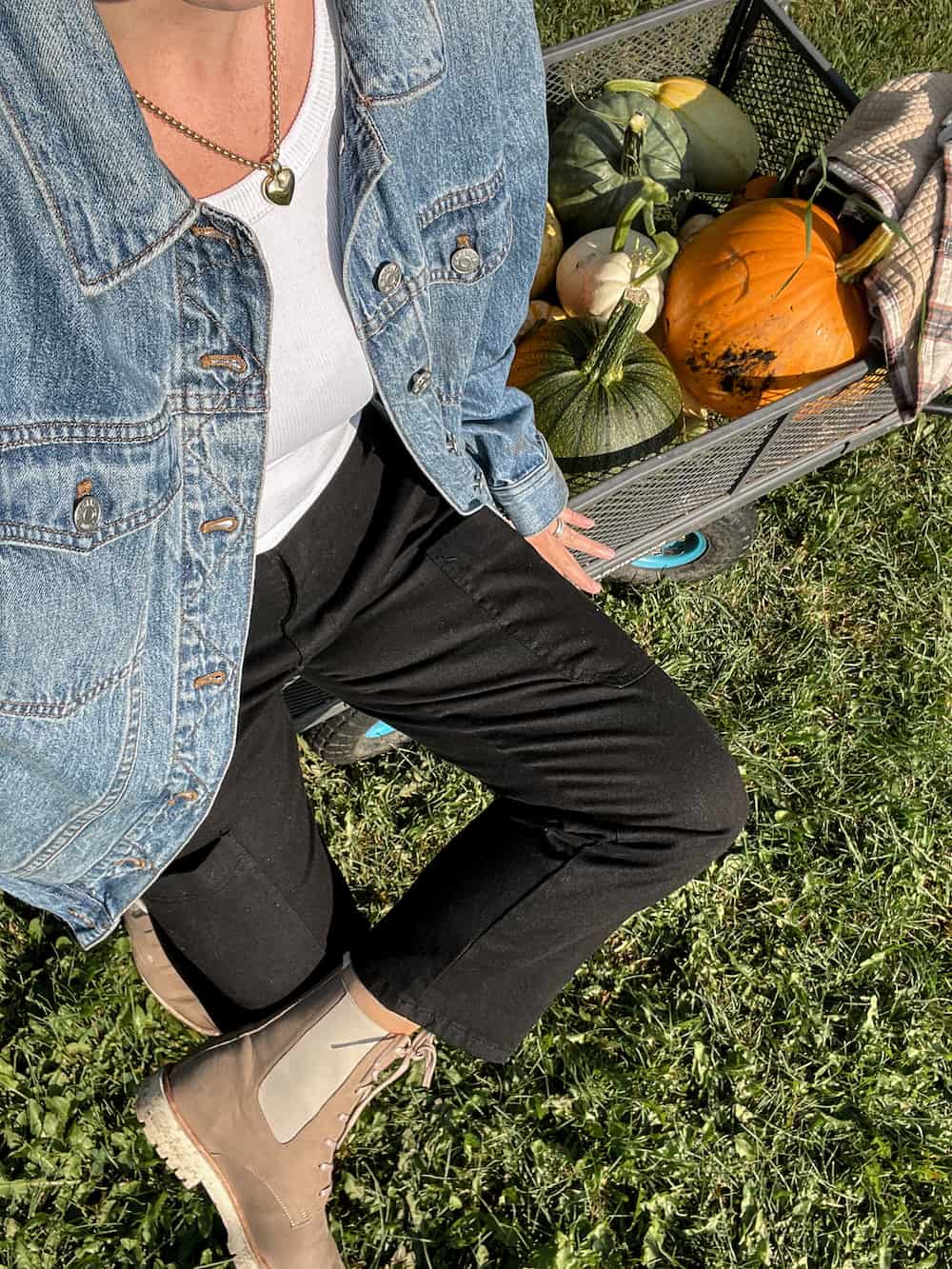 Woman wearing black jeans, tan chelsea boots, a white t-shirt and a denim jacket in a pumpkin patch.