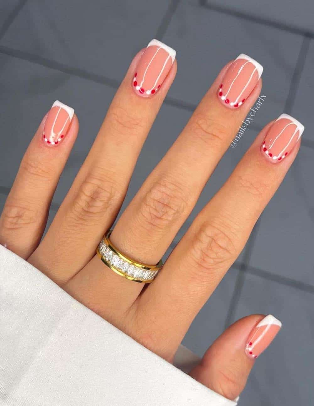 Manicura clásica con punta francesa en color blanco con detalle de puntos rojos y blancos.