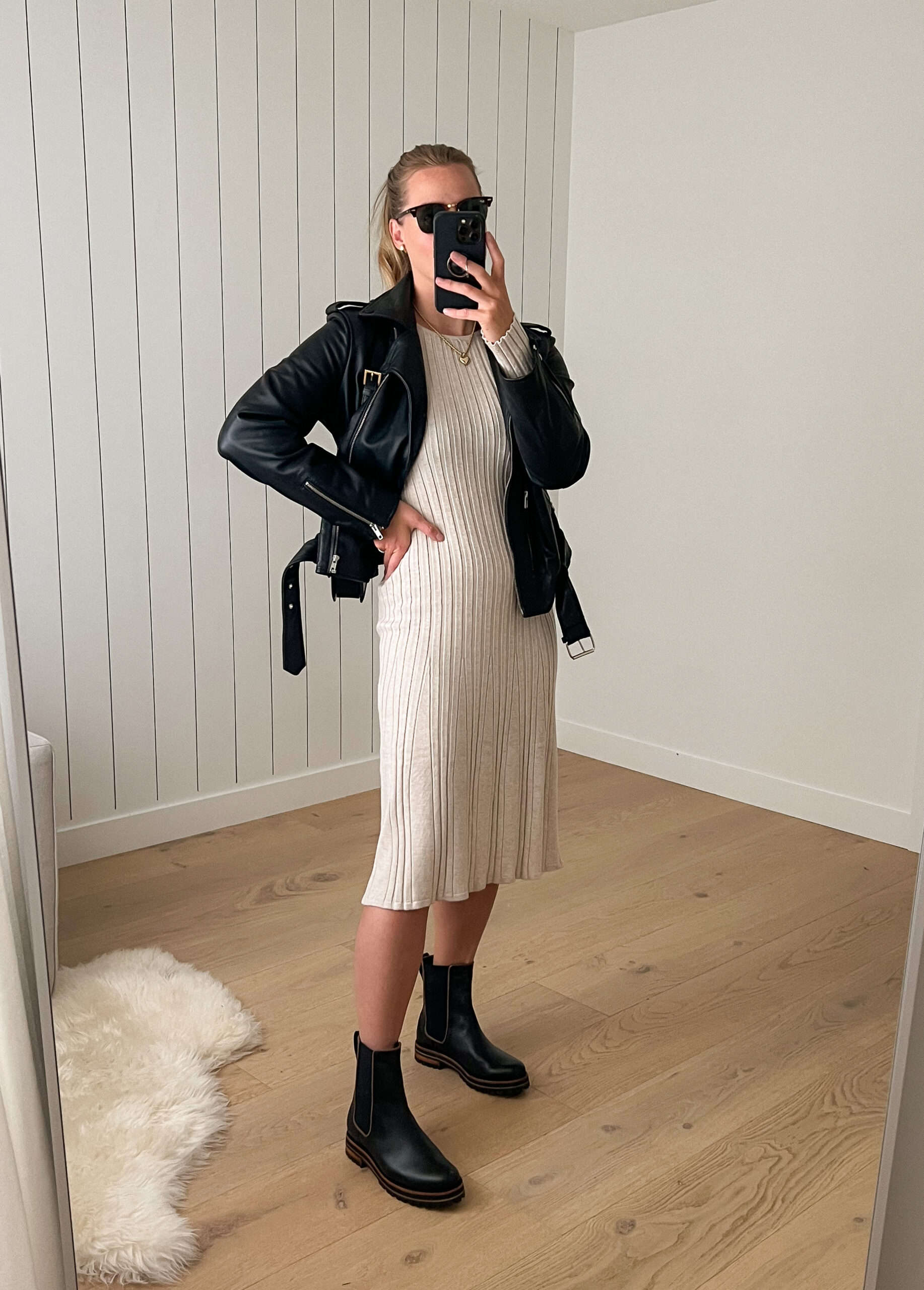 Woman wearing a cream sweater dress with black Chelsea boots and a black leather jacket.