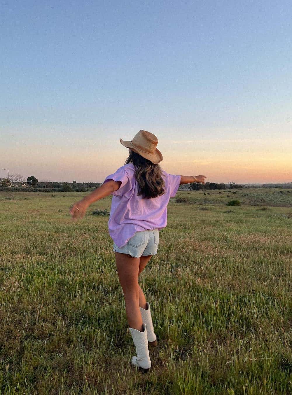 Woman wearing denim shorts and a purple t-shirt with white cowboy boots.