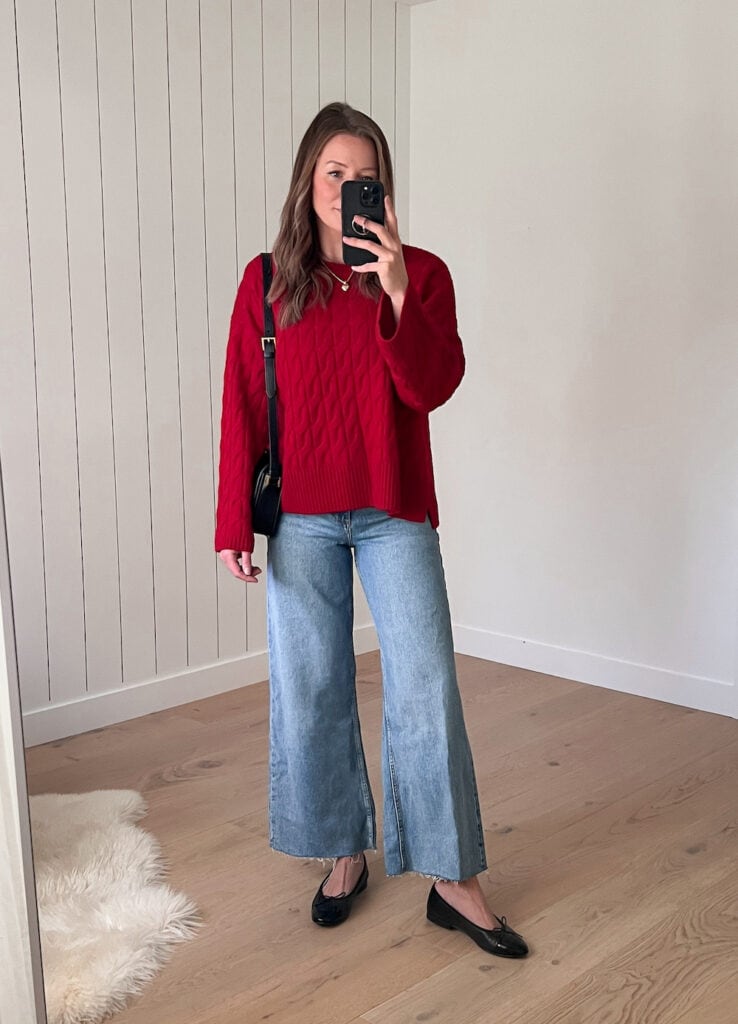 Woman wearing a chunky cable knit red sweater with wide leg jeans and black ballet flats