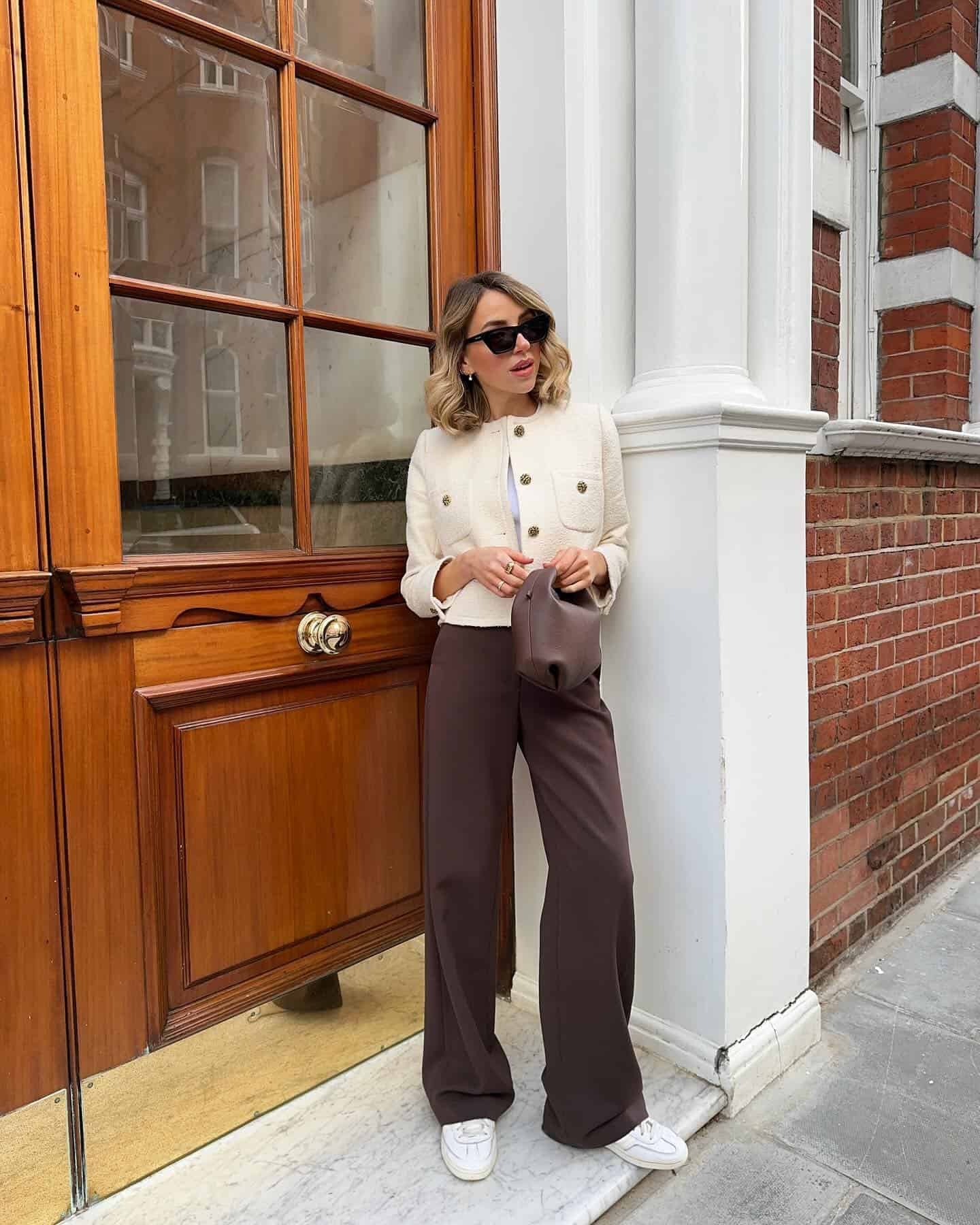 woman wearing a stylish outfit with a cropped cream tweed jacket and brown trousers with white sneakers