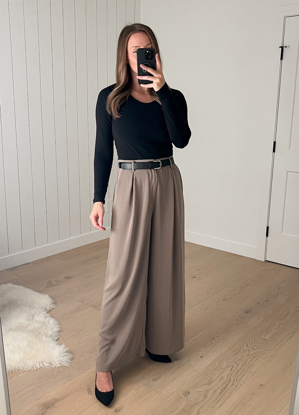 Christal wearing the wide-leg taupe pants with a black long-sleeved top and a black belt with black pumps