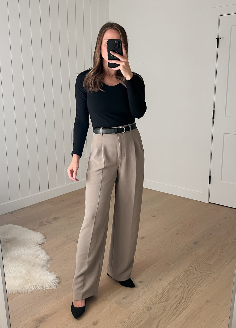 Christal wearing the Aritzia Effortless Pants in Nomad Taupe with a black long-sleeved top and a black belt with black pumps