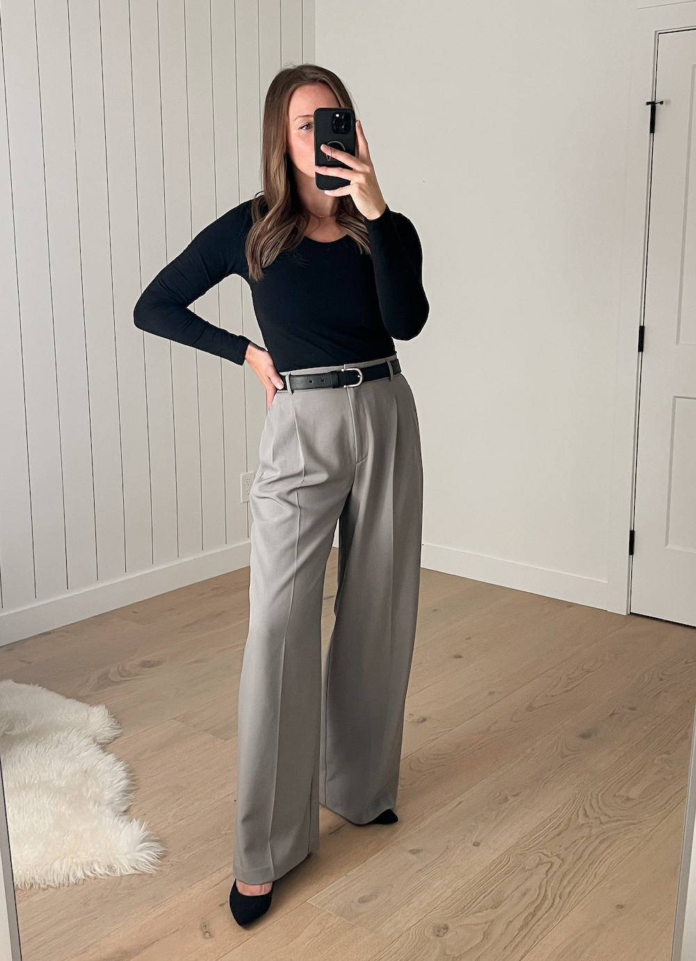 Christal wearing a black long-sleeved top with a pair of grey pleated wide leg pants and black suede pumps