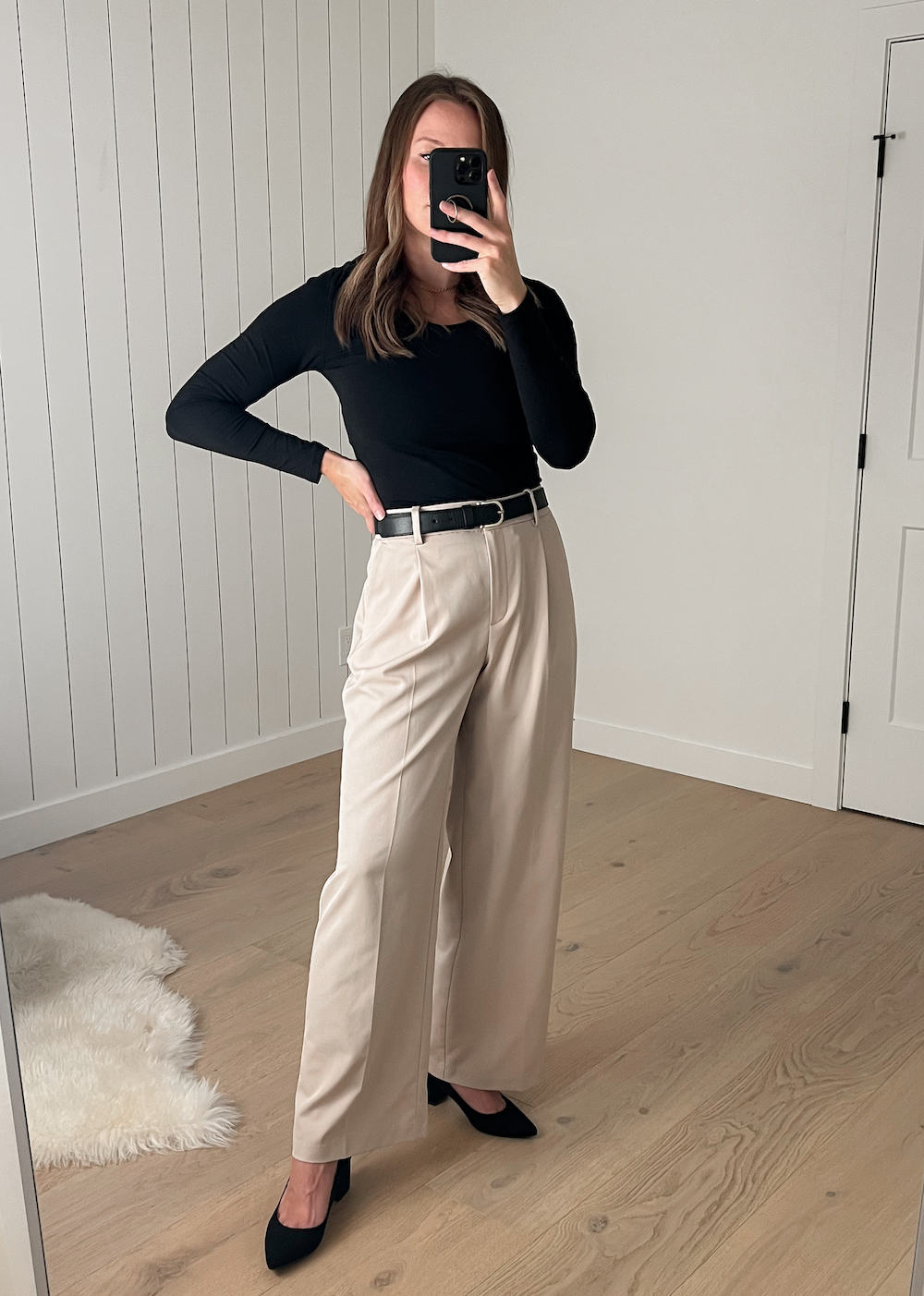 Christal wearing a black long-sleeved top with beige wide-leg pleated pants and black suede pumps