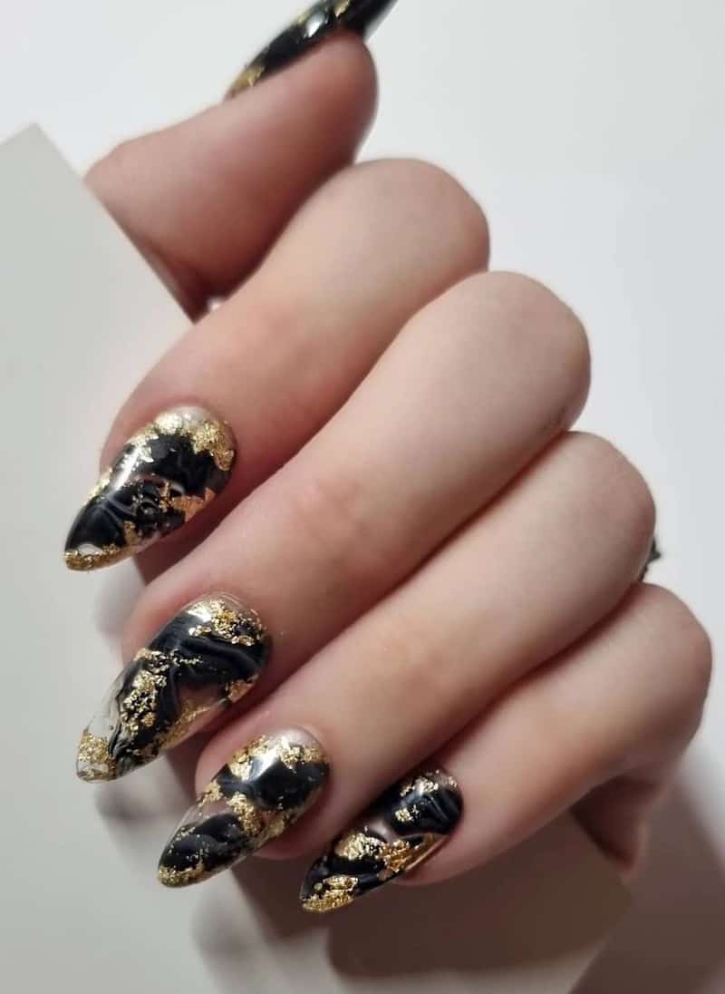 A hand with long almond nails with black marbled polish and gold foil