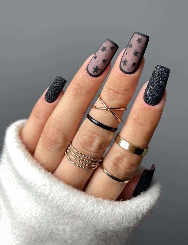 A hand with medium square nails painted a sparkling black with sheer black accent nails with stars