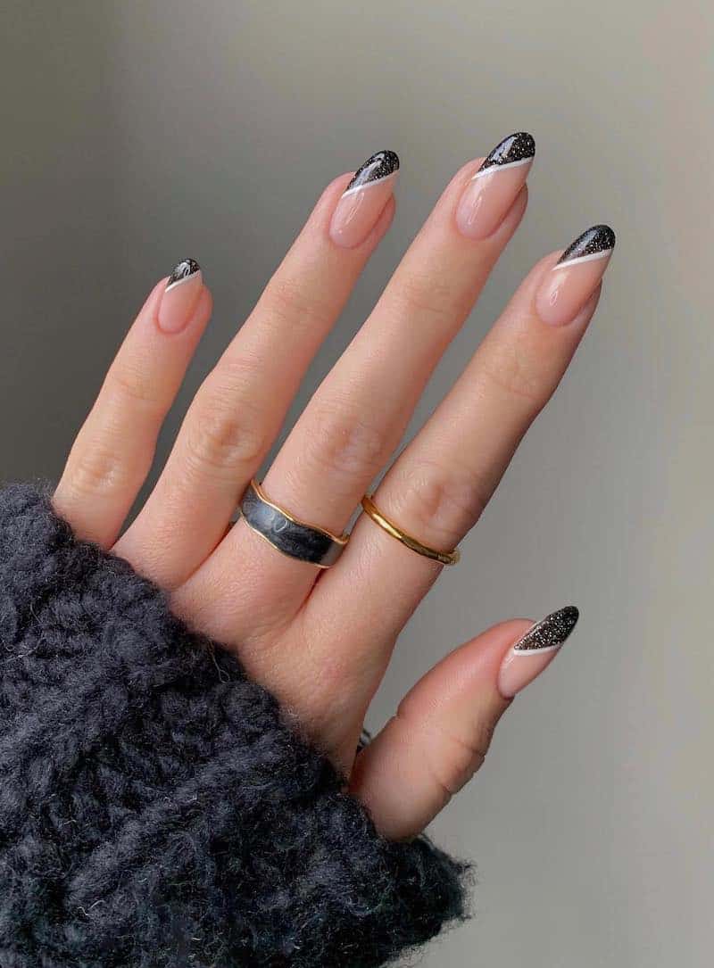 A hand with round nude pink nails with slanted sparkling black French tips with white borders