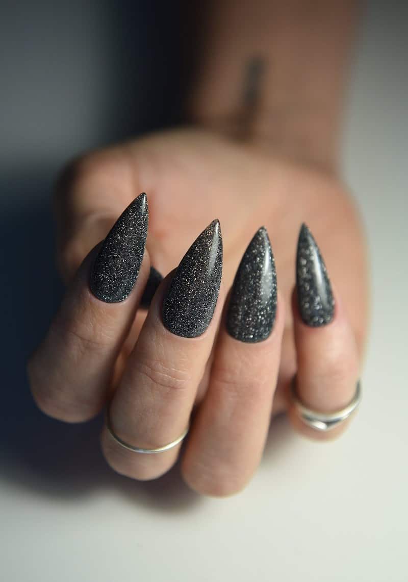 A hand with long stiletto nails painted with a sparkling black polish
