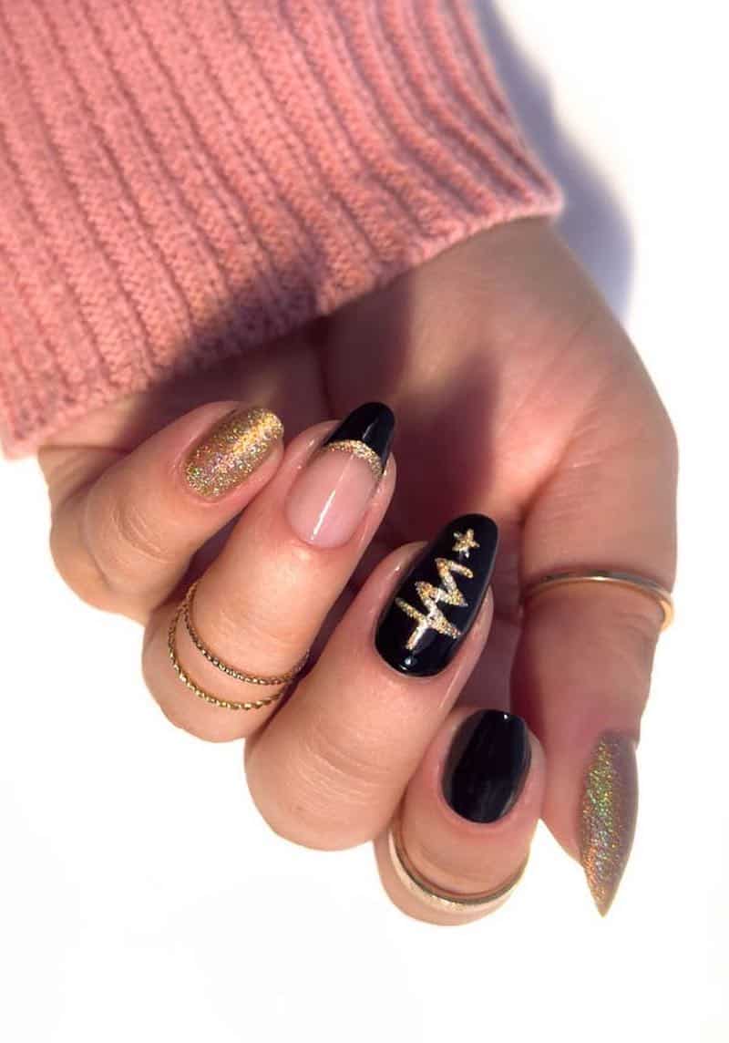 A hand with black and gold winter nails featuring French tips, gold glitter nails, and Christmas tree nail art