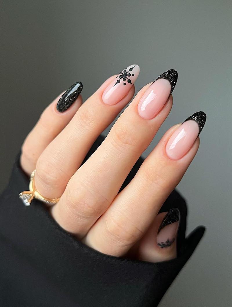 A hand with sparkling black French tips with black snowflake accents