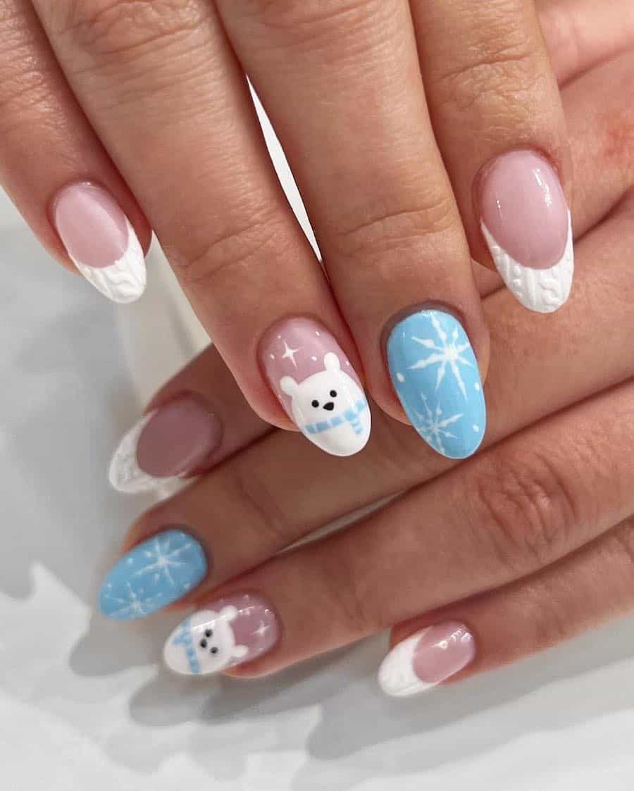 A hand with short almond nails painted in white sweater French tips with a blue accent nail with white snowflakes and a nude accent nail with polar bear nail art