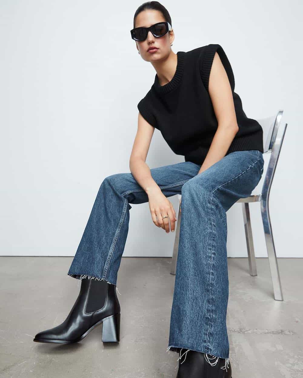 woman wearing a black sleeveless sweater with blue jeans and black boots from & Other Stories, a brand like Everlane