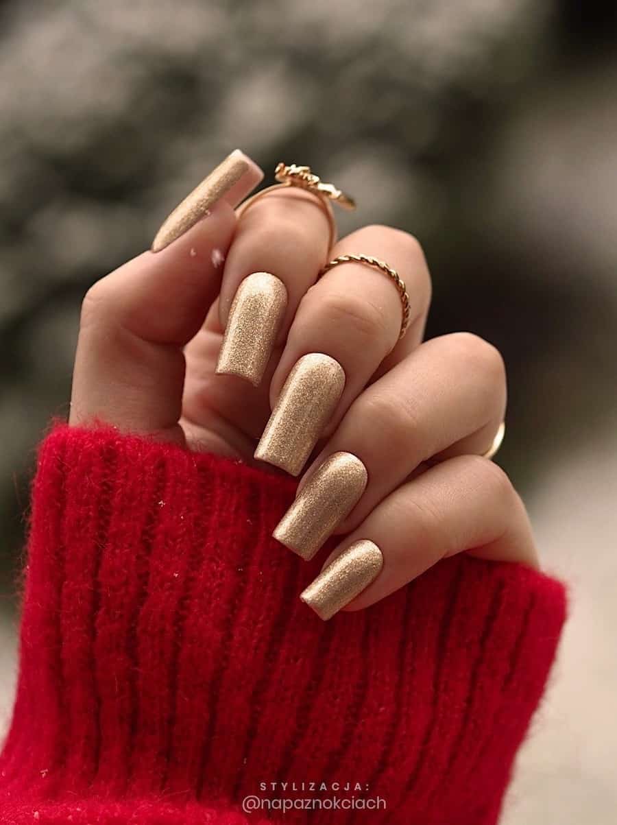 A hand with long square nails painted a gold glitter color
