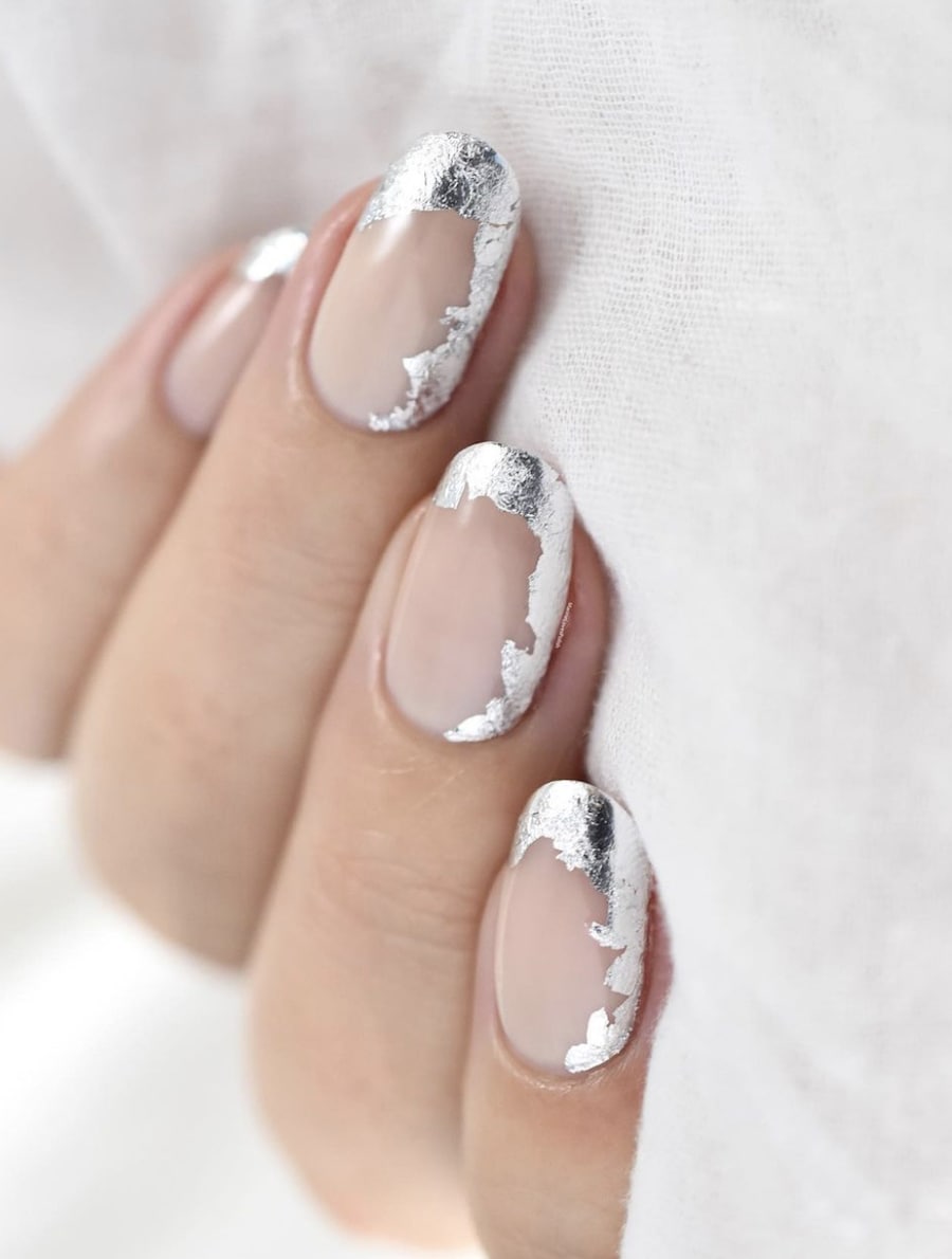 A hand with short round nails with silver flakes along the tips and one side of the nude nails