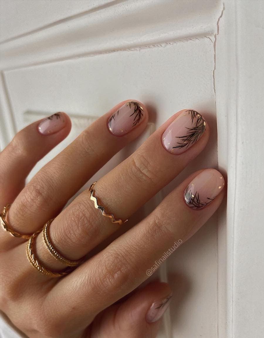 A hand with short round nails painted with a glossy topcoat with pine nail art and gold flakes