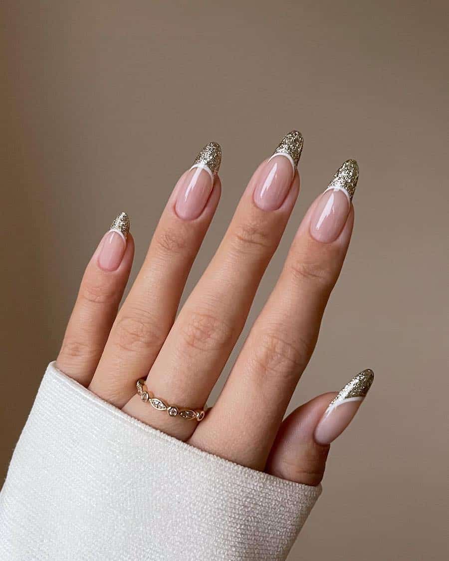 A hand with long glossy nude almond nails with gold glitter French tips and white borders