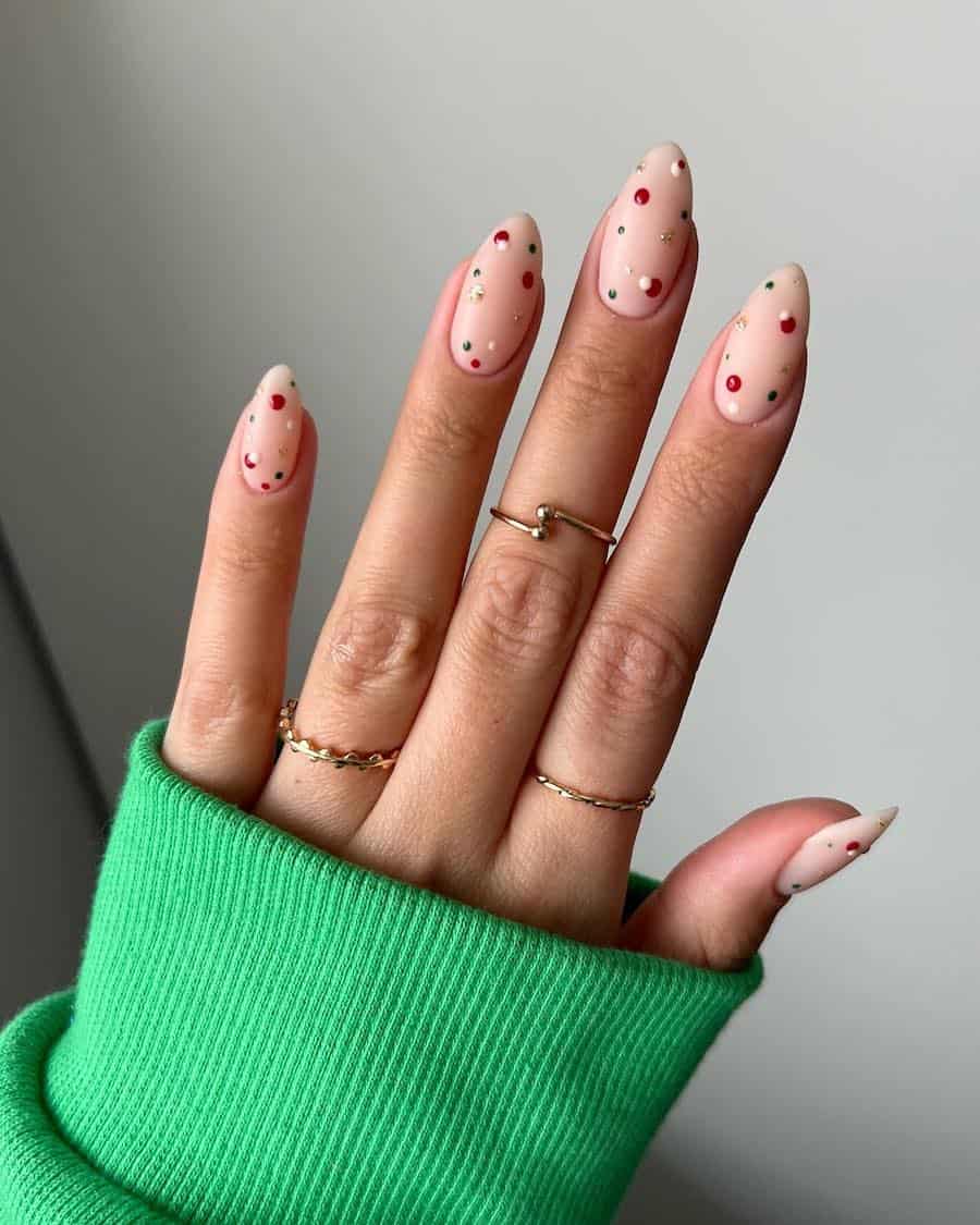A hand with short almond nails painted a matte nude with dots of red, green, white and gold glitter nail polish