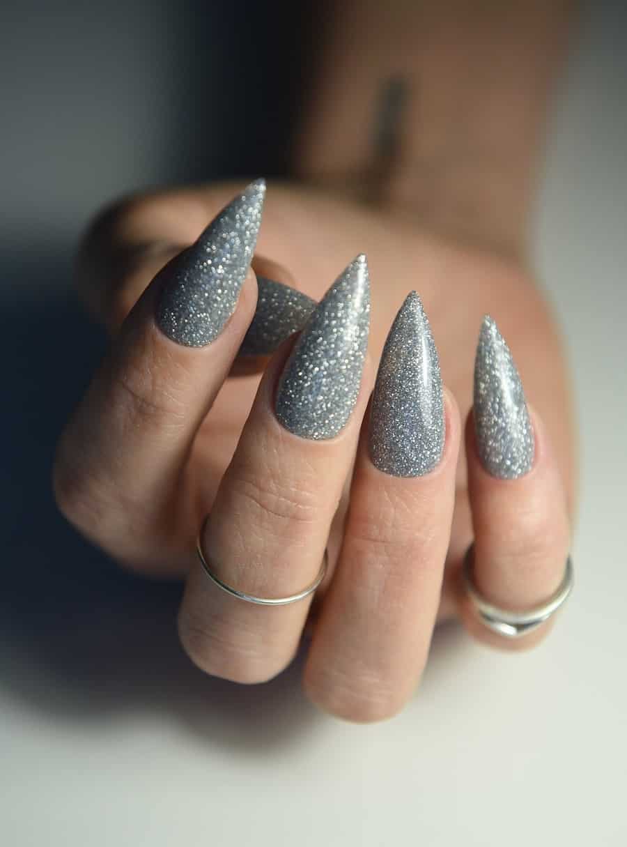 A hand with long stiletto nails painted with silver glitter nail polish