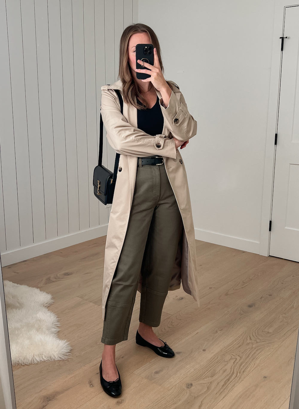 Christal wearing a long tan trench coat over a black top and green pants with black ballet flats