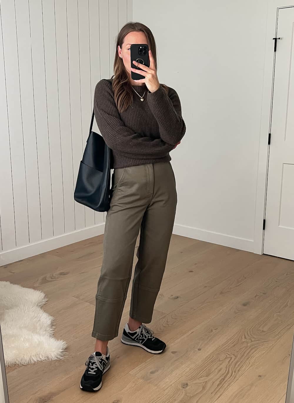 Christal wearing a dark brown knit sweater with olive green pants and black New Balance sneakers